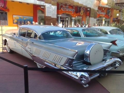 1991 Ford LTD Crown Victoria - Vintage cars are parked outside a Disney Store, with one car a spare tire mounted on its rear.