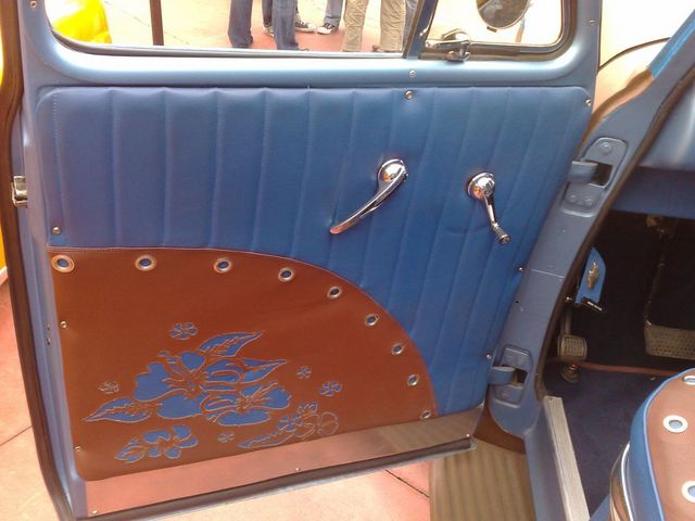 Car interior door panel with blue tufted upholstery and a brown lower section with floral cutouts