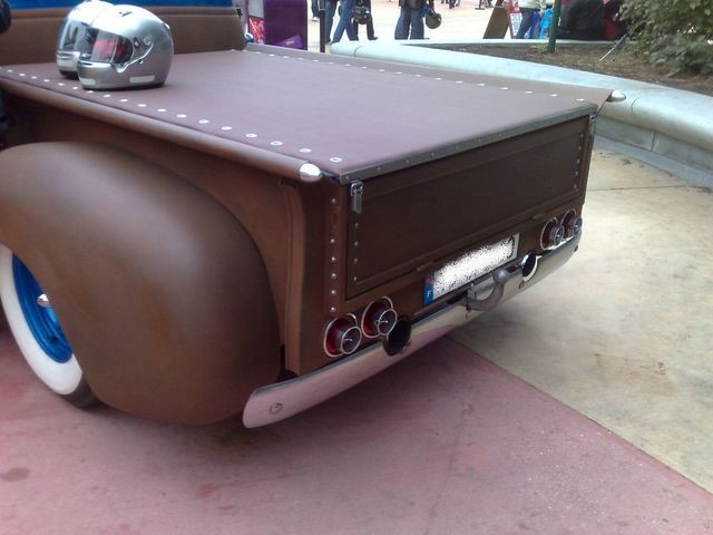 Brown customized pickup truck bed with a tonneau cover and two helmets on top. Chrome bumper and exhaust pipes visible