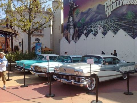 1991 Ford LTD Crown Victoria - A trio of vintage automobiles are displayed outdoors, with a colorful mural serving as a backdrop.