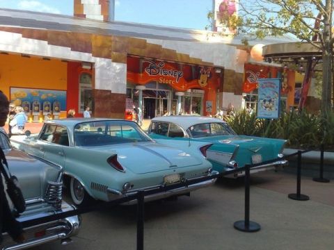 1991 Ford LTD Crown Victoria - Two classic cars are parked in front of a Disney Store, with one car in the foreground and another behind it.