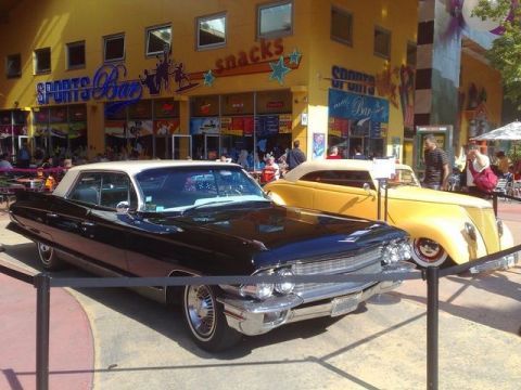 1991 Ford LTD Crown Victoria - A black 1963 coupe with a white roof is parked in front of a yellow convertible, with a sports bar in the background.