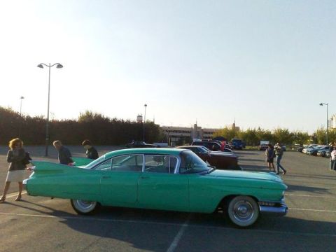 1991 Ford LTD Crown Victoria - A classic green Cadillac with distinctive tail fins is parked in a lot with other vehicles.