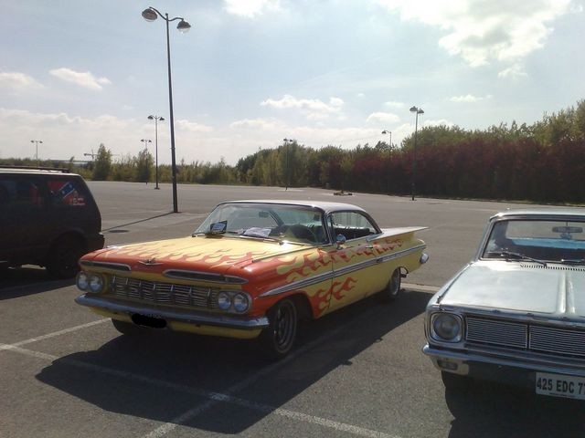 Yellow and orange 1959 Chevrolet Impala coupe with flame decals parked in a lot