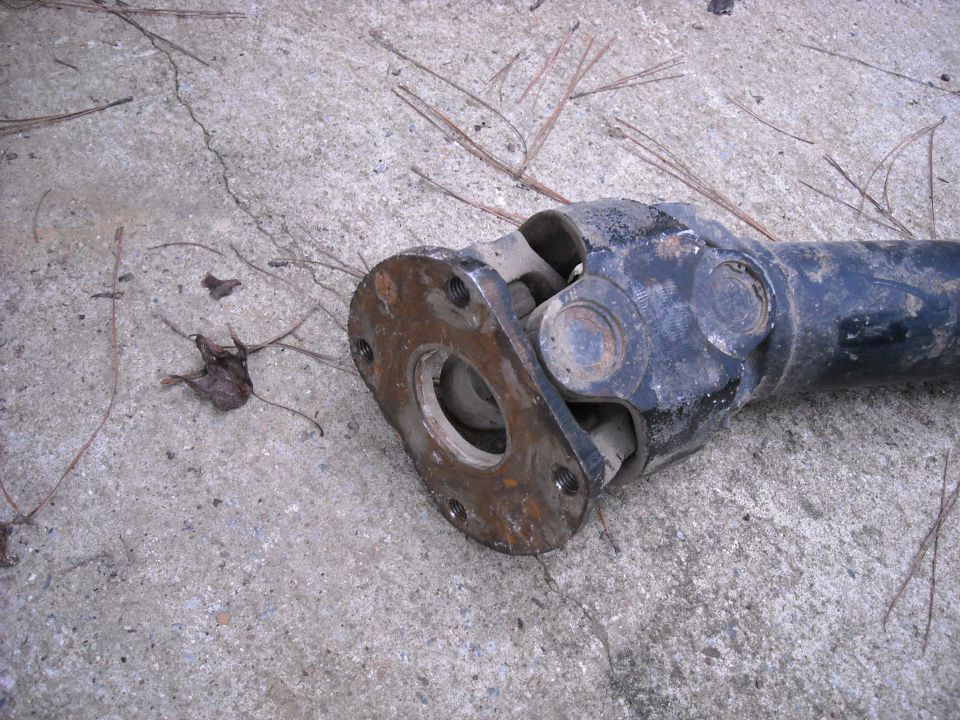 Driveshaft U-joint and flange on concrete with pine needles and a dead leaf
