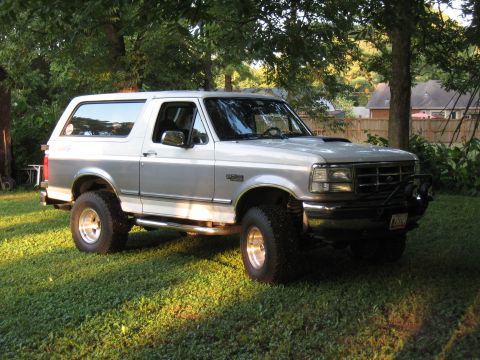 1994 Ford Bronco - This lifted Ford Bronco features a two-tone paint scheme and is parked on a grassy lawn.