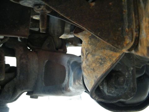 1982 Ford Bronco - Close-up view of the vehicle's undercarriage, revealing rusty suspension parts and a rubber boot.