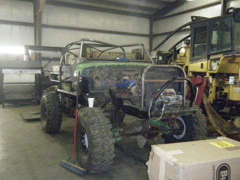 1978 Ford Bronco - A heavily modified vehicle with a roll cage and oversized tires is in a workshop, with other heavy equipment visible.