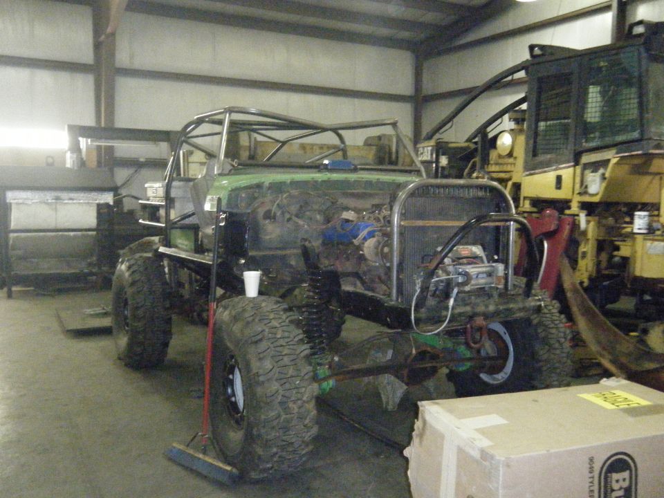 custom off-road vehicle build with roll cage, large tires, and exposed engine, parked next to heavy machinery