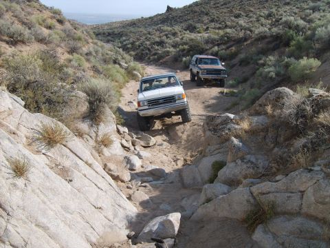 1989 Ford Bronco - Two SUVs navigate a challenging rocky trail in a desert landscape.
