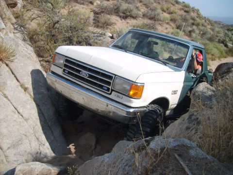 1989 Ford Bronco - This truck is off-roading over large rocks on a dry, hilly landscape.