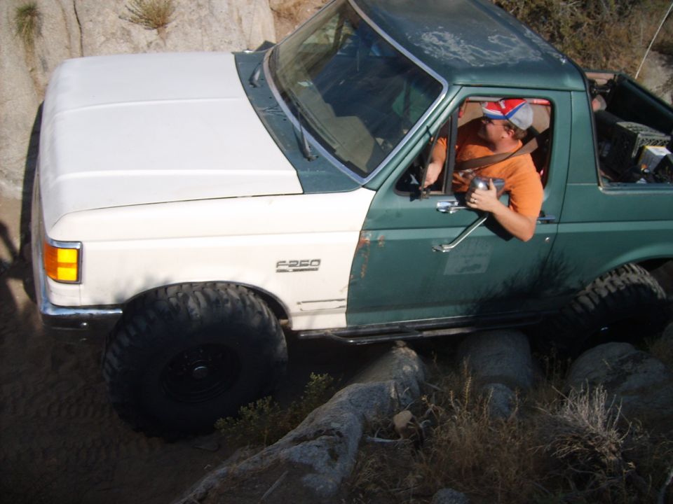 Ford F-250 off-roading over rocks, driver in orange shirt and hat