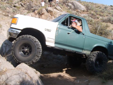 1989 Ford Bronco - This modified truck, likely from the early 1990s, is shown tackling a rocky trail with a driver giving a thumbs-up.