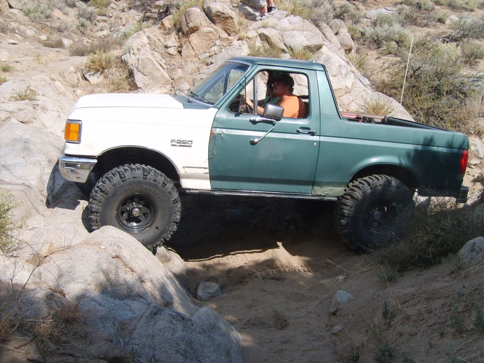 1989 Ford Bronco off-roading on rocks, white front fender, green cab and rear