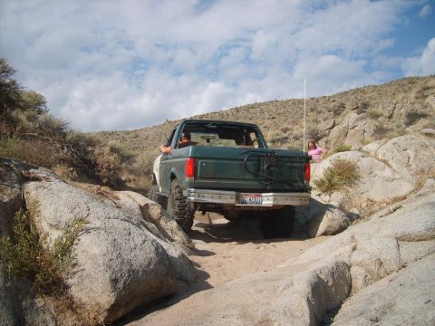 1989 Ford Bronco - A green Ford Bronco navigates a challenging rocky terrain under a partly cloudy sky.