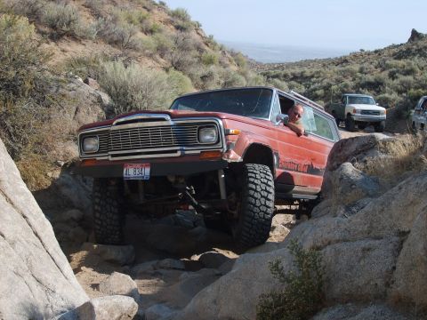 1989 Ford Bronco - A red Jeep Wagoneer navigates a rocky trail with other vehicles following.