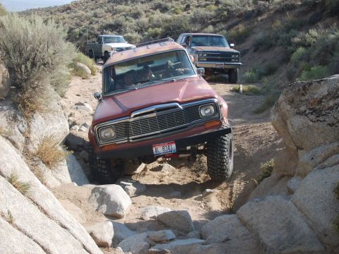 1989 Ford Bronco - A convoy of off-road vehicles, led by a red Jeep Wagoneer, tackles a challenging rocky trail.