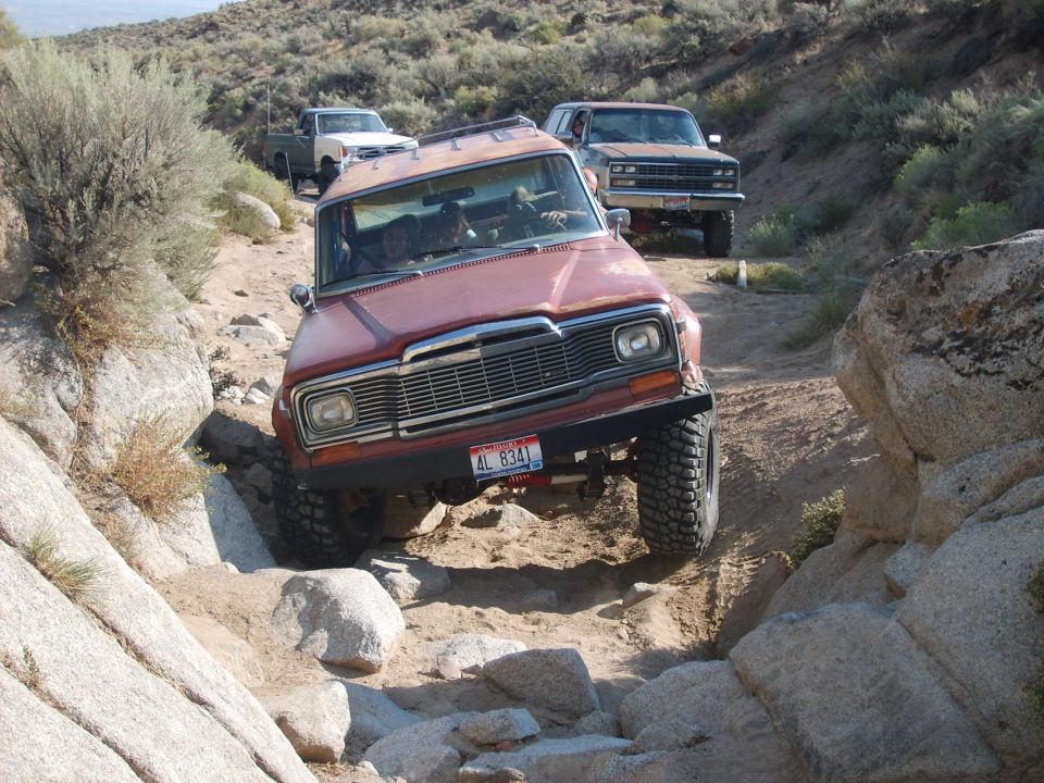 Red Jeep Wagoneer navigating rocky terrain, AL 8341 license plate visible
