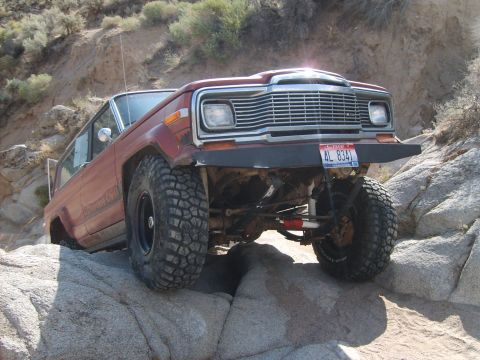 1989 Ford Bronco - This lifted Jeep Wagoneer is navigating a rocky trail with large off-road tires.