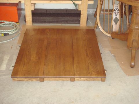 1988 Ford F-150 - A wooden table top is laid out on a concrete floor, with various household items and furniture parts in the background.