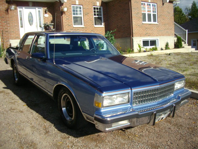 Blue 1980s Chevrolet Caprice sedan front three-quarter view on gravel drive