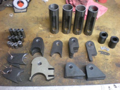 Suzuki Samurai - A collection of custom metal fabrication parts, including tabs and sleeves, are arranged on a workbench.