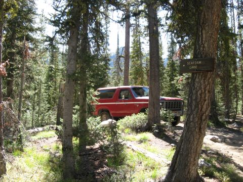 1981 Ford Bronco - A red Ford Bronco is parked off a dirt road in a wooded area, near a sign for Seafoam Lake.