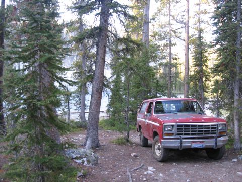1981 Ford Bronco - A red Ford Bronco is parked in a wooded area next to a lake.