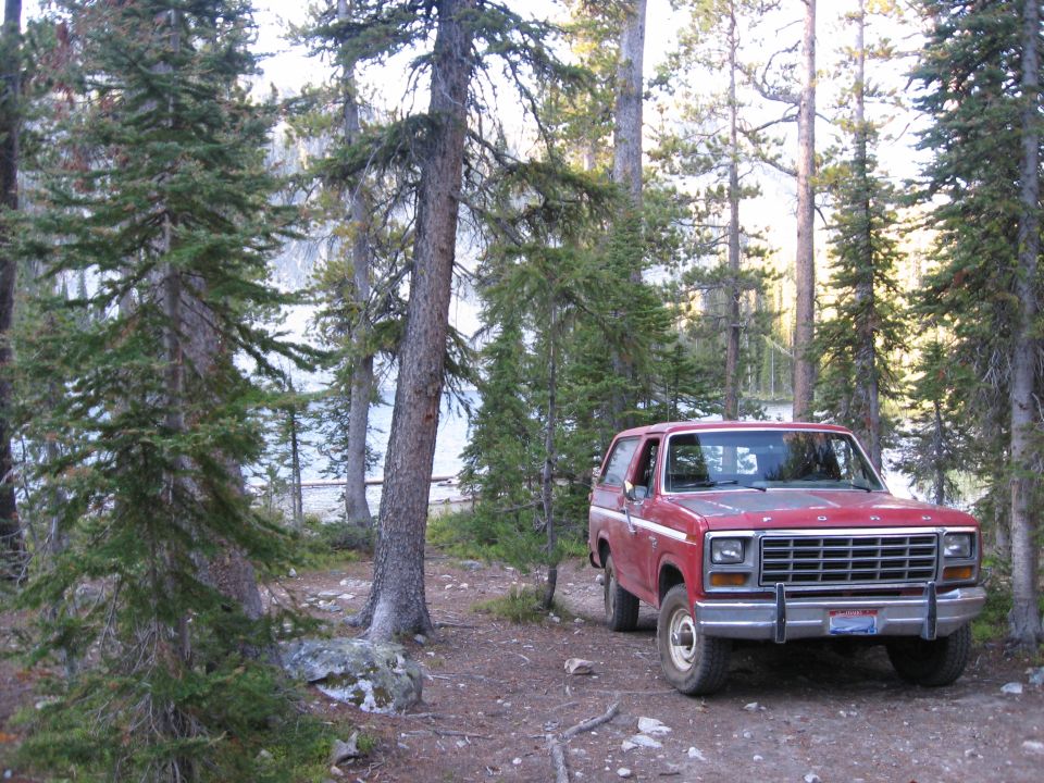 Red Ford Bronco parked in a forest clearing near a lake