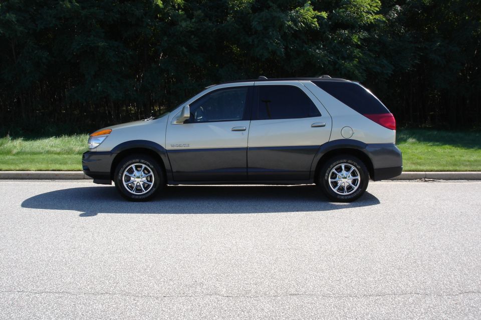Gold and gray Buick Rendezvous SUV in side profile on a sunlit road