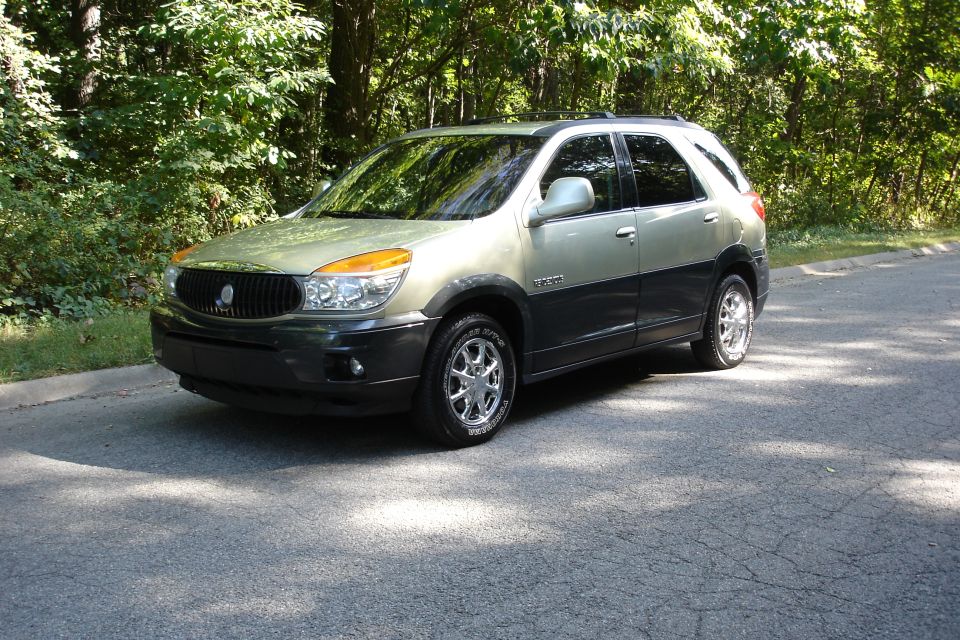 Sage-green crossover SUV, front three-quarter view, on a wooded road