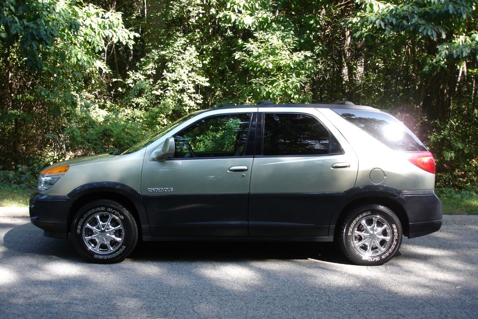Gold Buick Rendezvous SUV side profile with Yokohama white-letter tires on wooded road