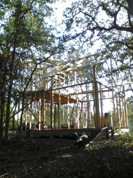 1996 Ford Bronco - Construction of a wooden house frame is underway amidst trees, with workers present on site.