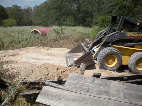 1996 Ford Bronco - A New Holland skid steer loader is positioned on a dirt pile, with a large red pipe visible in the background.