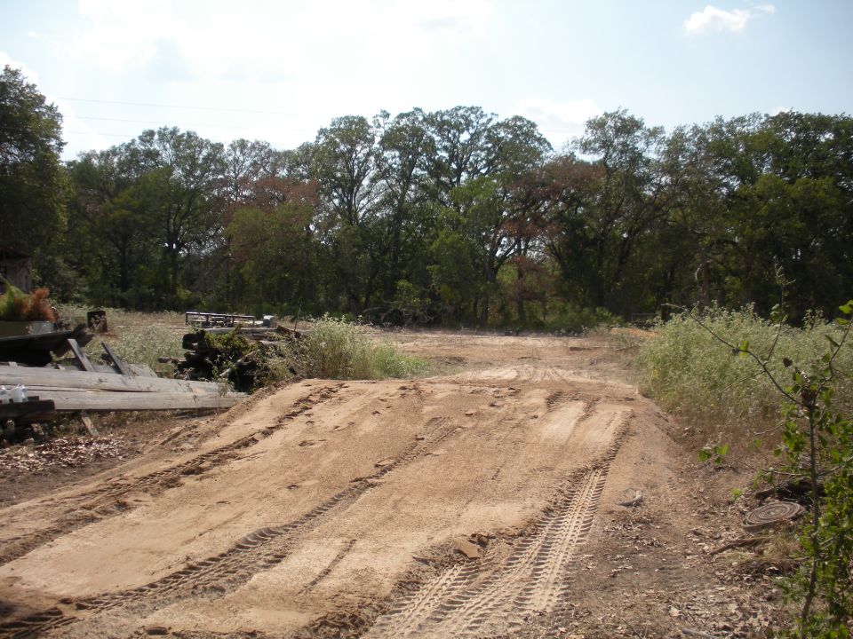 dirt track with tire marks, trees in background, some debris on left