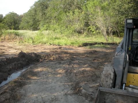 1996 Ford Bronco - A skid steer loader is partially visible in a muddy, disturbed outdoor area with trees in the distance.