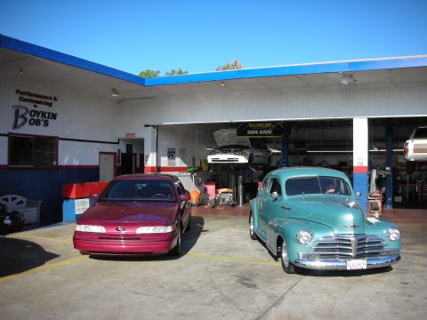 1992 Ford Crown Victoria - Two cars, a red sedan and a teal vintage vehicle, are parked in front of a garage with "Boykin Bob's" signage.