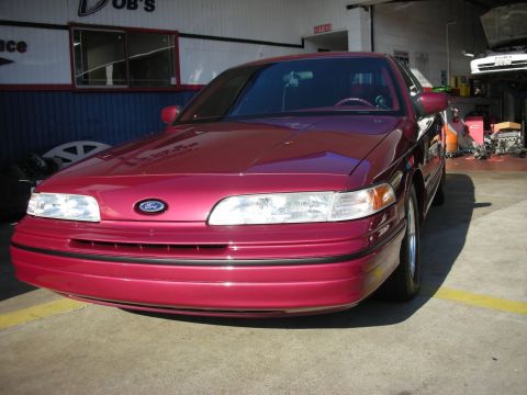 1992 Ford Crown Victoria - A red 1992 Ford Crown Victoria is parked in front of an open garage bay.