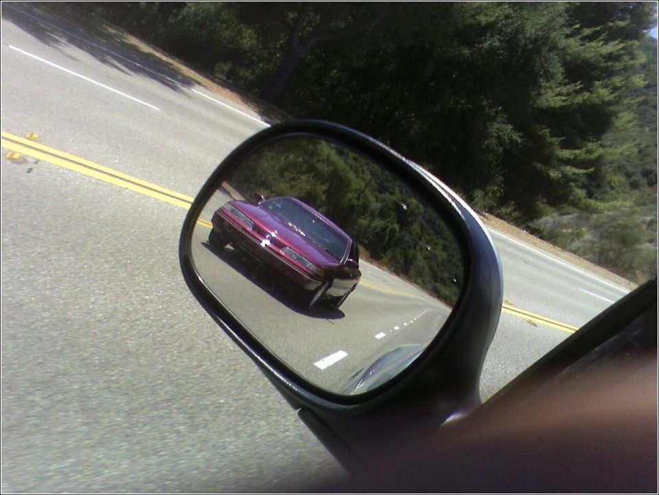 Purple sedan reflected in side mirror, seen from a 3/4 front angle