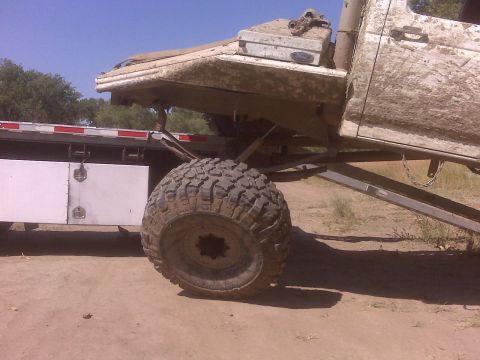 1992 Ford F-350 - A heavily mud-splattered pickup truck is shown from the side, equipped with large off-road tires and parked next to a flatbed trailer.