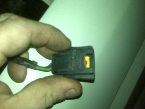 1995 Ford Bronco - A hand holds a black electrical connector with yellow and red markings, likely a vehicle part.