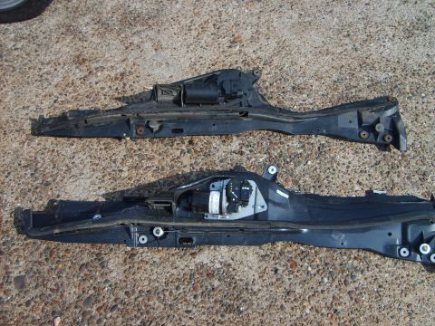 1993 Ford Crown Victoria - Two black automotive parts, possibly from a car's chassis or body, are laid out on a textured surface.