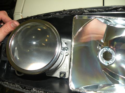 1998 Subaru Legacy - A person is holding a projector lens for a car headlight assembly, showing the internal components.