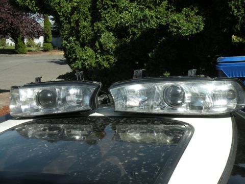1998 Subaru Legacy - Two car headlights are displayed on the reflective surface of a car's sunroof, with trees and a street in the background.