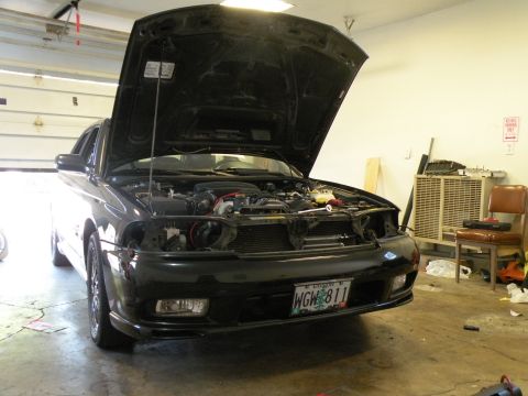 1998 Subaru Legacy - The front of a black 1998 Subaru Legacy is shown with its hood open, revealing the engine bay and a license plate.