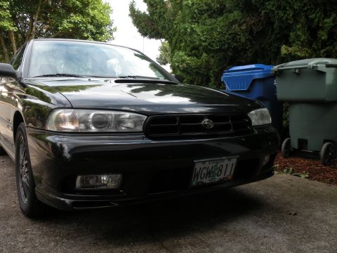 1998 Subaru Legacy - The front grille and headlights of a black Subaru Legacy are visible, parked in a driveway.