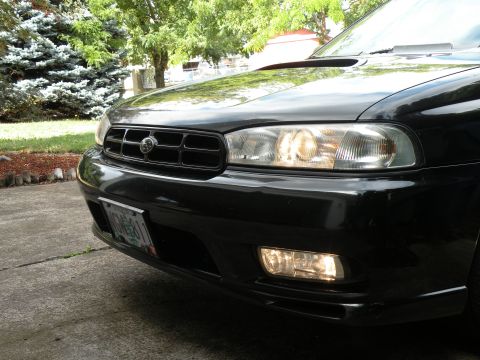 1998 Subaru Legacy - Front view of a black 1998 Subaru Legacy, showing its grille and illuminated lights.
