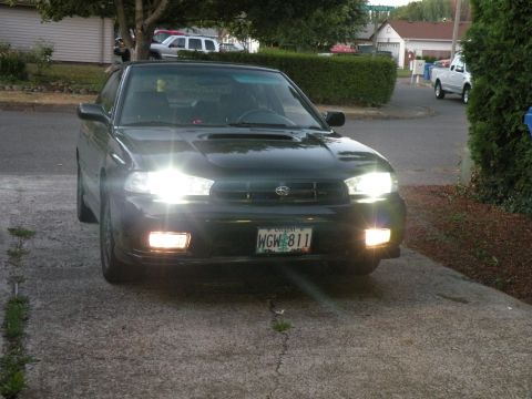 1998 Subaru Legacy - Front view of a 1998 Subaru Legacy sedan, parked in a driveway with headlights illuminated.