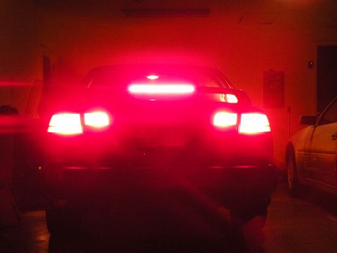 1998 Subaru Legacy - The rear of a car is shown with its brake lights on, illuminating the scene in red. A second vehicle is partially visible to the right.