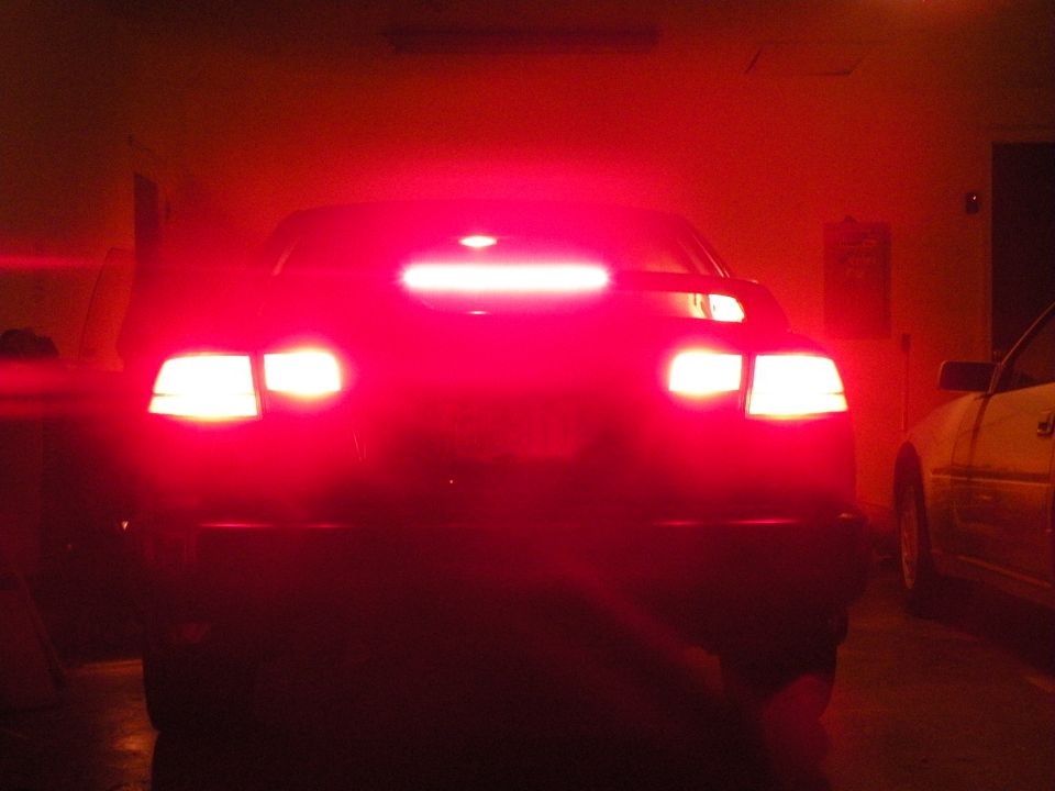 Rear view of a car with bright red brake lights illuminated. Another car is visible to the right